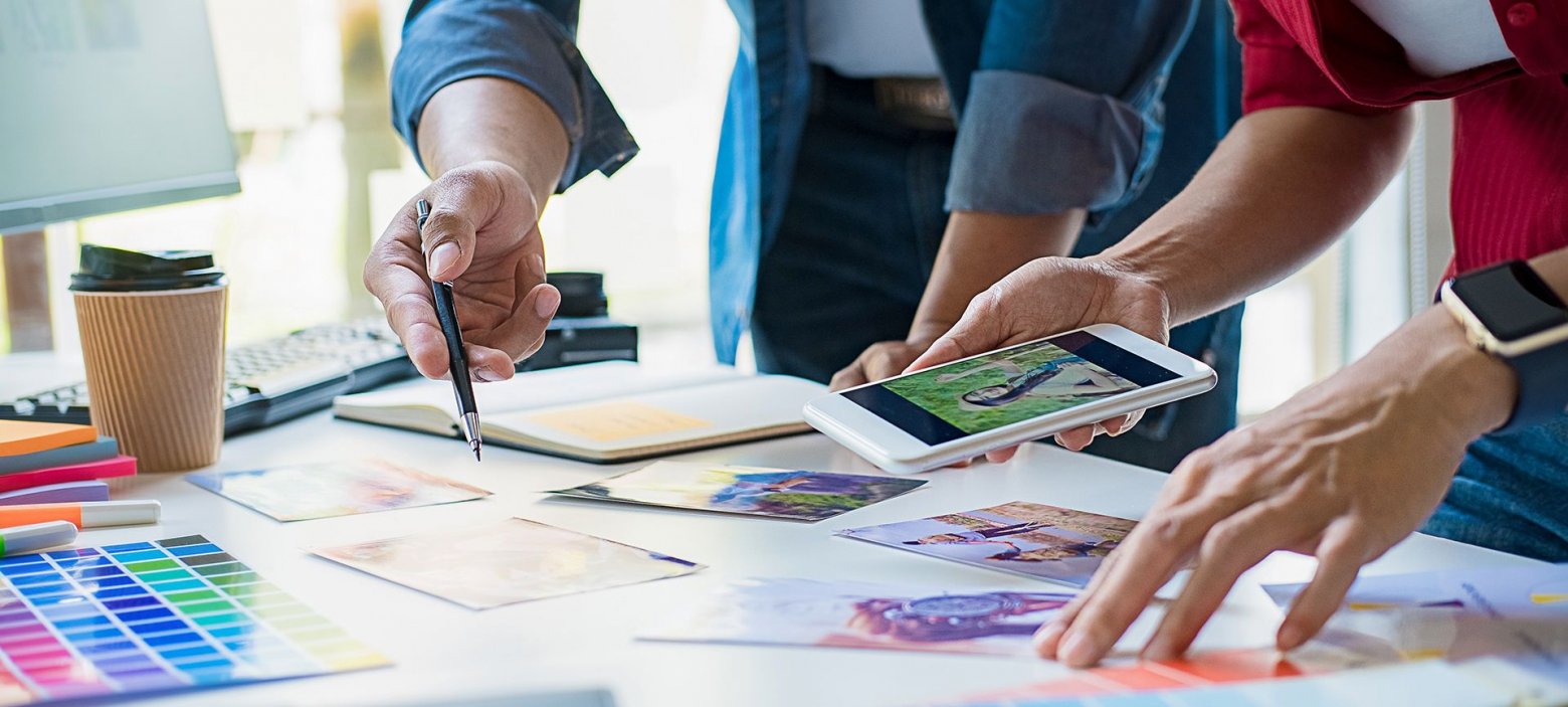 Mehrere Personen arbeiten gemeinsam an einem Projekt mit verschiedenen Materialien wie Papier, einem Smartphone und einem Farbmuster.